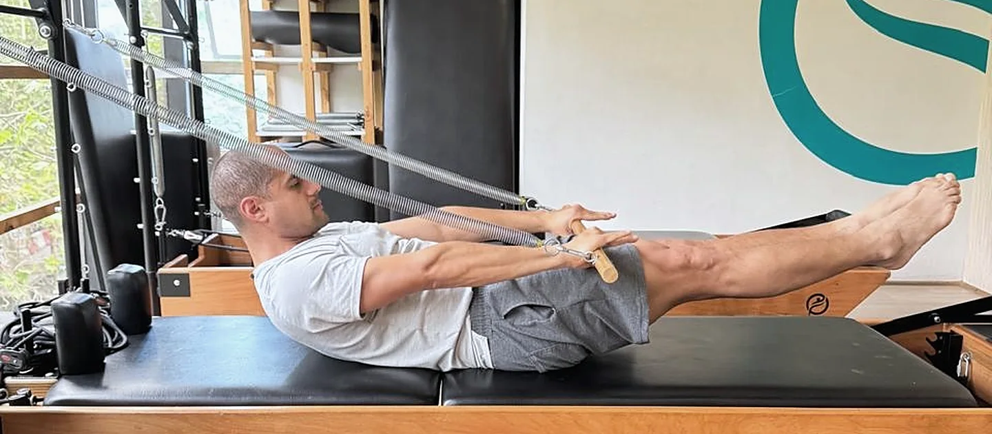 Alumno de Enjoy Pilates en un ejercicio sobre el reformer, con el mural del estudio al fondo