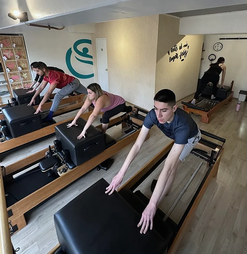 Clase de cinco alumnos sobre reformers en la sala de Enjoy Pilates, con el mural del estudio al fondo