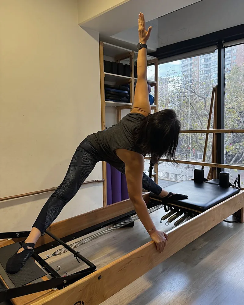 Alumna de Enjoy Pilates en una postura de Pilates sobre el reformer, frente al ventanal del estudio