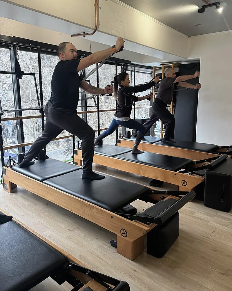 Tres alumnos de Enjoy Pilates entrenando con las correas de la torre sobre sus reformers